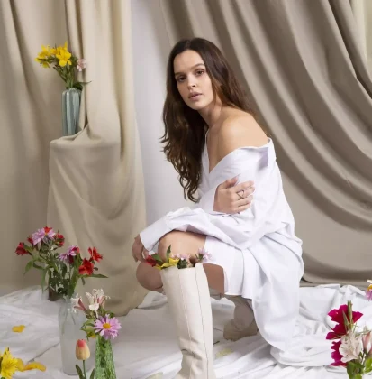 Modelo con vestido blanco y flores al rededor.